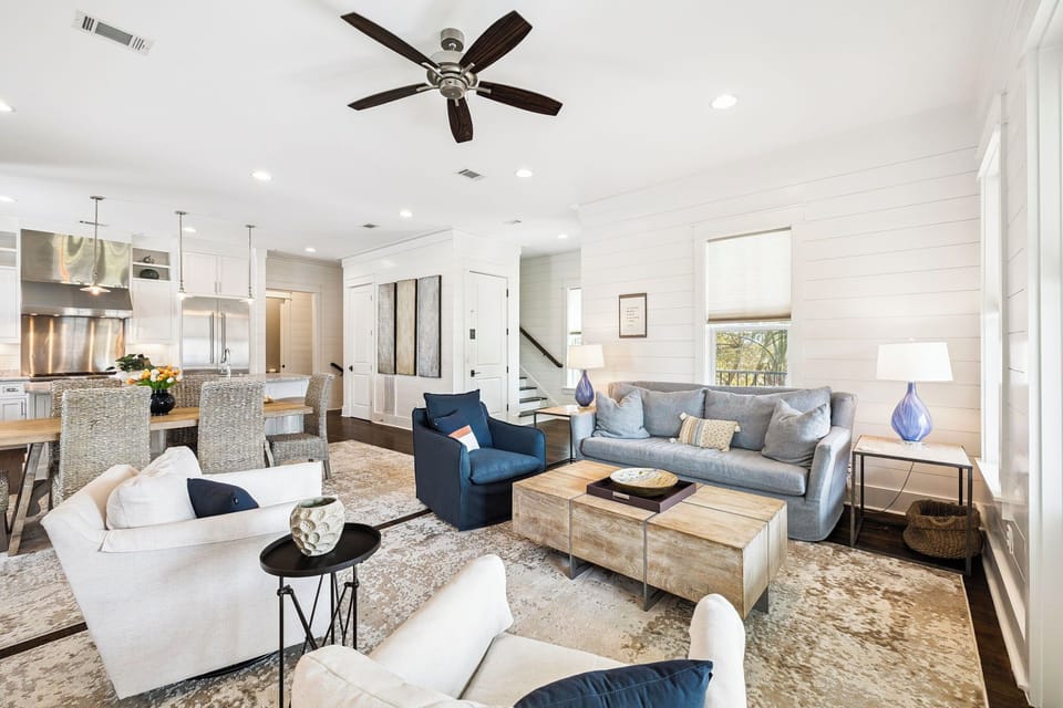 Settle into your bright, open-plan living room where plush sofas invite relaxation. Shiplap walls, a cozy ceiling fan, and sunlight through large windows create the perfect setting to unwind.
