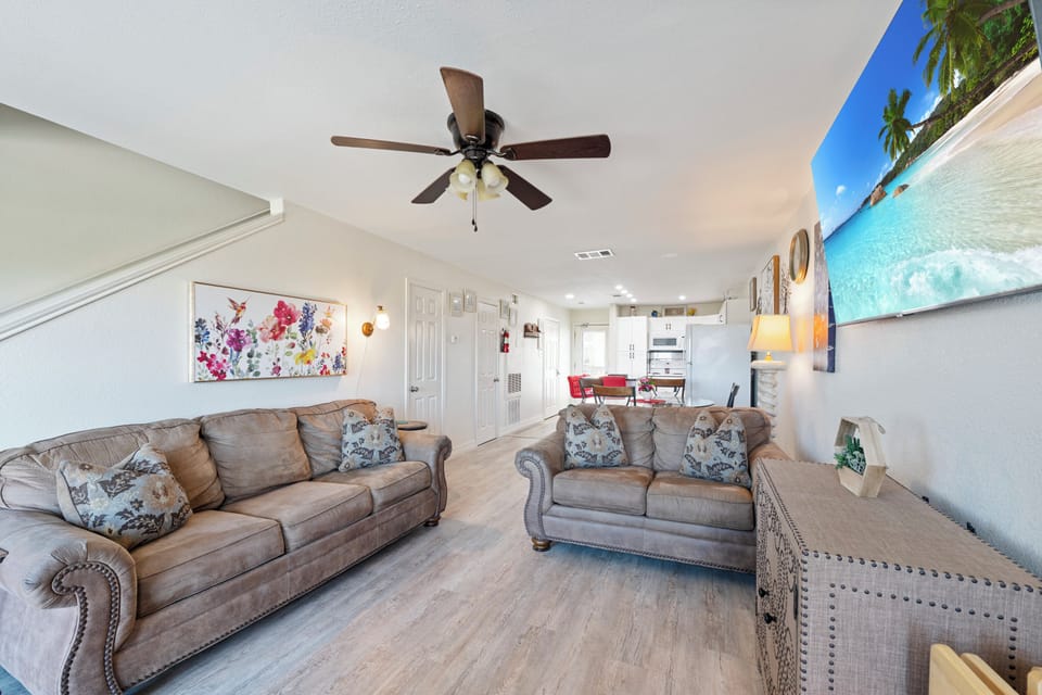 Unwind in your spacious living area with plush seating, tropical artwork, and a ceiling fan keeping you cool.
