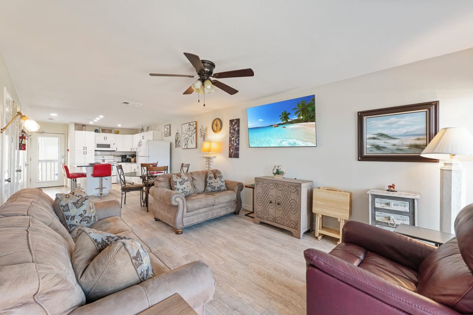 Relax in your spacious living area with plush seating, tropical artwork, and an open kitchen perfect for family meals.