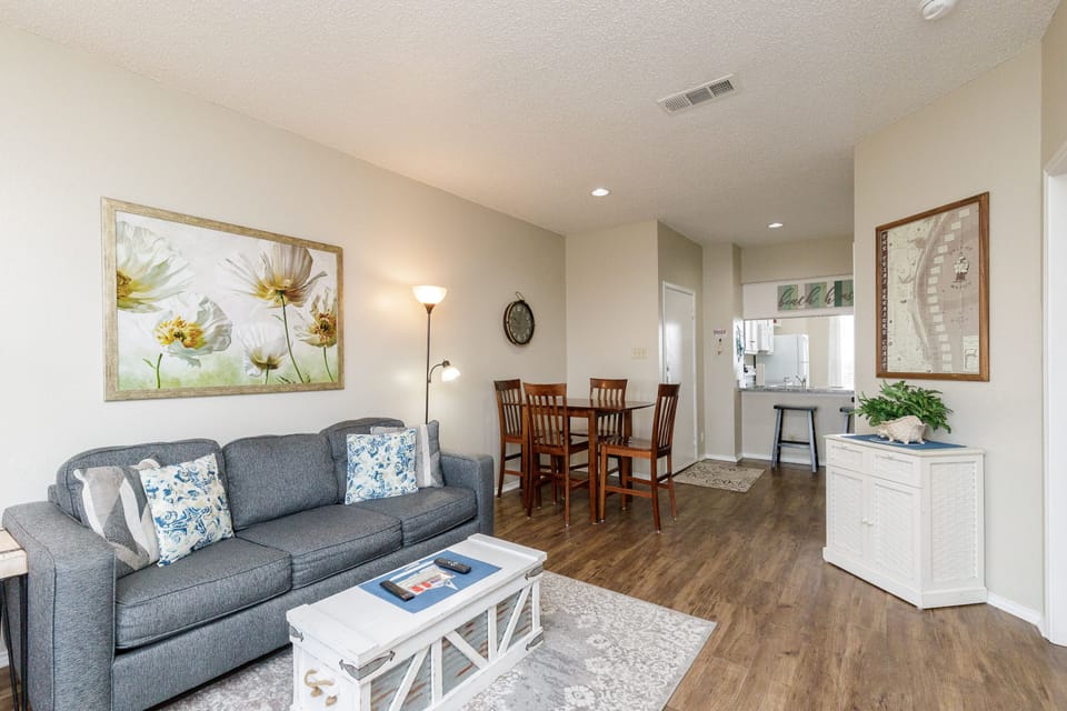 Relax in your bright, open living space featuring a cozy gray sofa, elegant dining area, and thoughtful touches like fresh flowers and local artwork.