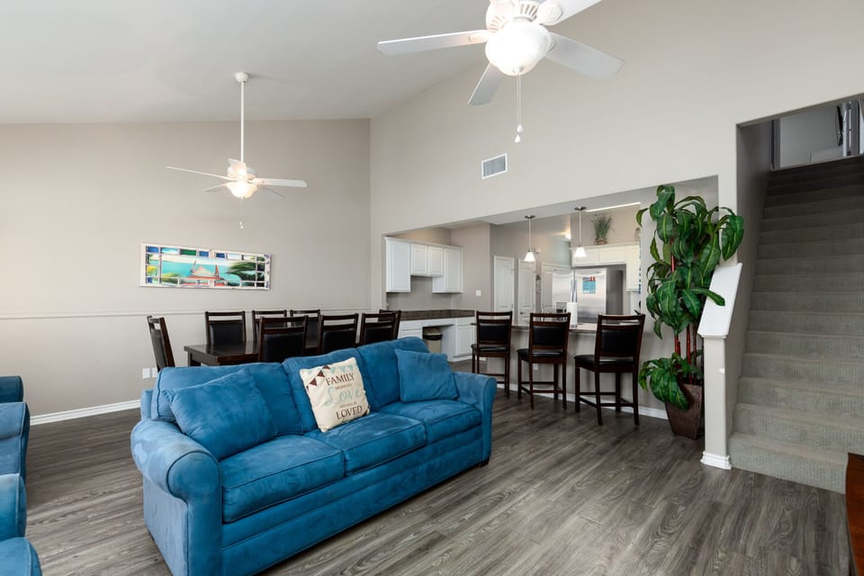 Relax in your spacious open-concept living area with comfortable blue seating, modern kitchen, and elegant dining space perfect for group gatherings.