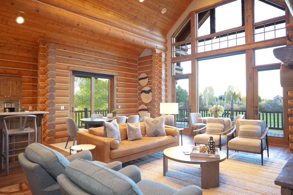 Step into your stunning log cabin retreat where soaring ceilings and floor-to-ceiling windows flood the space with natural light. Sink into plush seating by the warmth of rustic timber walls while enjoying sweeping views of the lush countryside through pan