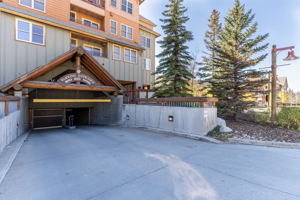 The property features a covered parking entrance with convenient access, surrounded by mature evergreen trees and mountain landscaping.
