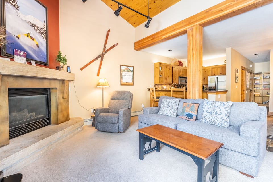 Cozy up by the stone fireplace in your mountain retreat's living room, where rustic wood beams and ski-themed decor create perfect après-ski ambiance.
