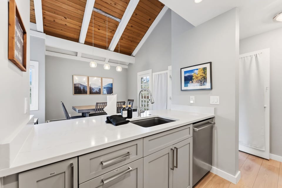 The kitchen features lovely white countertops and light-colored cabinets, stainless steel appliances, and an open kitchen bar with two bar stools overlooking the dining and living room.