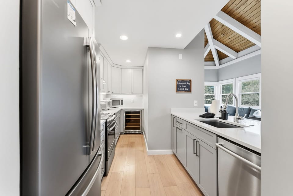 The kitchen features lovely white countertops and light-colored cabinets, stainless steel appliances, and an open kitchen bar with two bar stools overlooking the dining and living room.