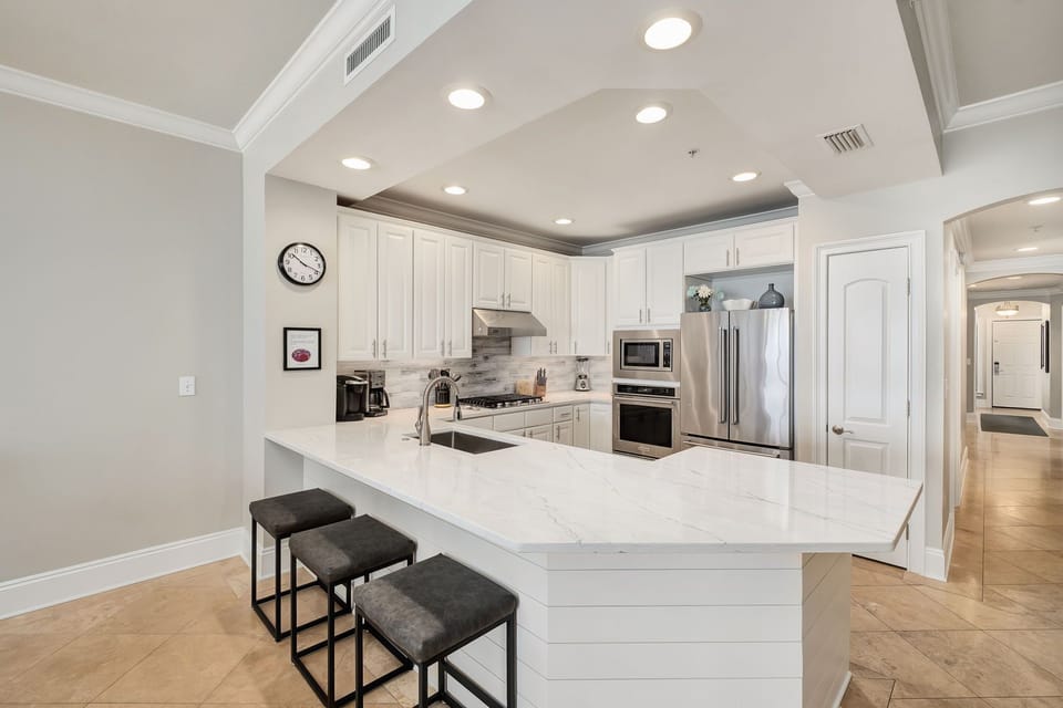 Your fully-equipped kitchen sparkles with modern stainless appliances, sleek white cabinetry, and a spacious island perfect for preparing home-cooked meals or gathering with loved ones.