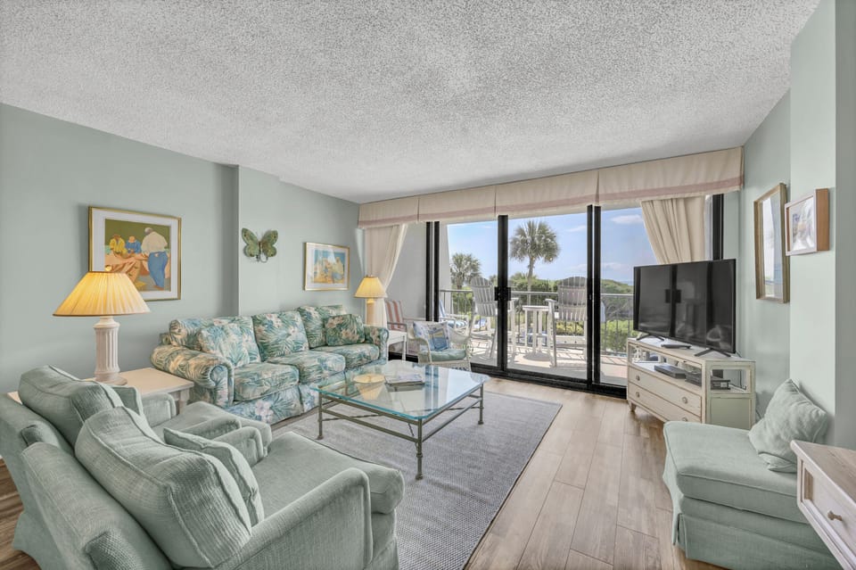 Sink into plush coastal seating with a refreshing drink as you gaze out at swaying palms and lush greenery through your private balcony doors.