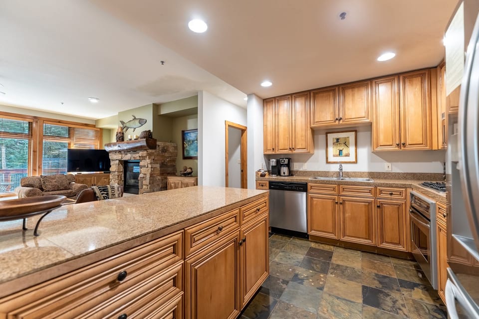 Your gourmet kitchen features granite countertops, rich wood cabinetry, and stainless steel appliances, flowing seamlessly into the cozy living area with stone fireplace.