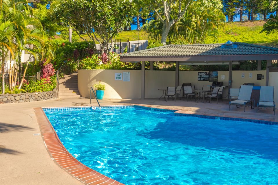 Sparkling blue waters invite you to relax under swaying palms while comfortable loungers and shaded seating await poolside, surrounded by lush tropical greenery.