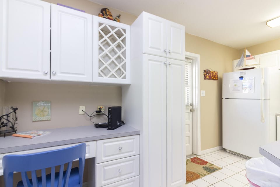 Built-in desk area with white cabinetry, wine rack, gray laminate countertop, and a blue wooden chair.