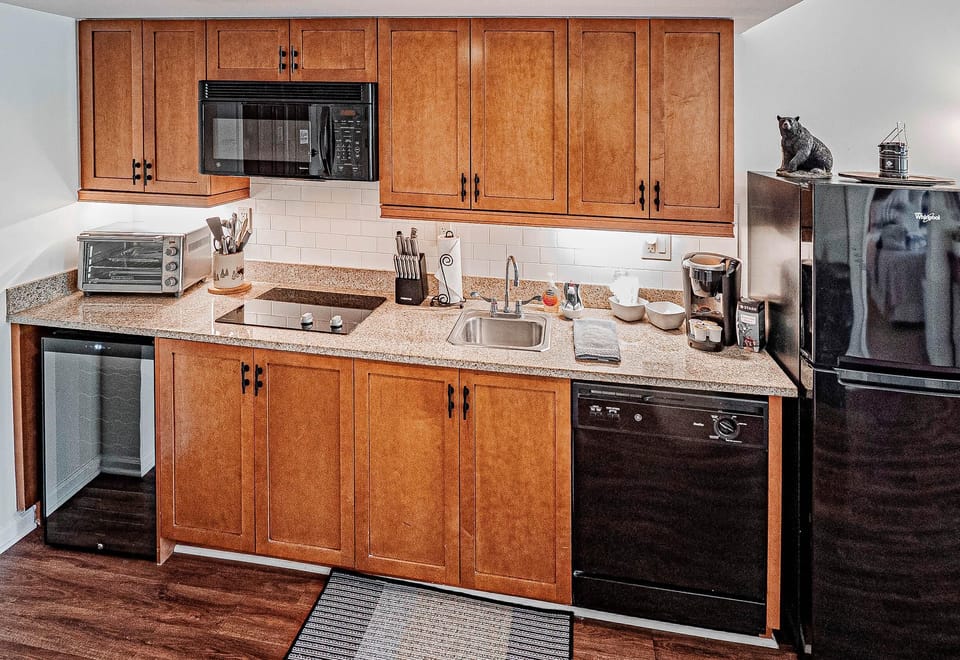 Galley kitchen with ice maker, ceramic glass stove top, microwave, Keurig, Pots and pans, utensils, dishware, and near full size fridge