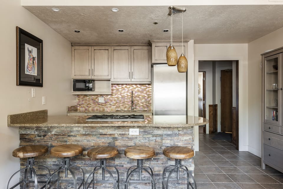 Slate tile kitchen bar with wooden swivel barstools for 5, unique pendant drop lighting and stainless steel appliances in the kitchen