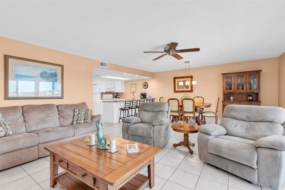 Relax in your open-concept living space with plush seating, ceiling fan, and seamless flow into the dining area and well-equipped kitchen—perfect for memorable gatherings.