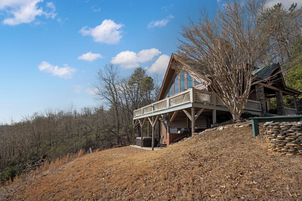 A charming mountain cabin nestled on a hillside, featuring rustic wood architecture and a spacious deck overlooking the forested landscape.