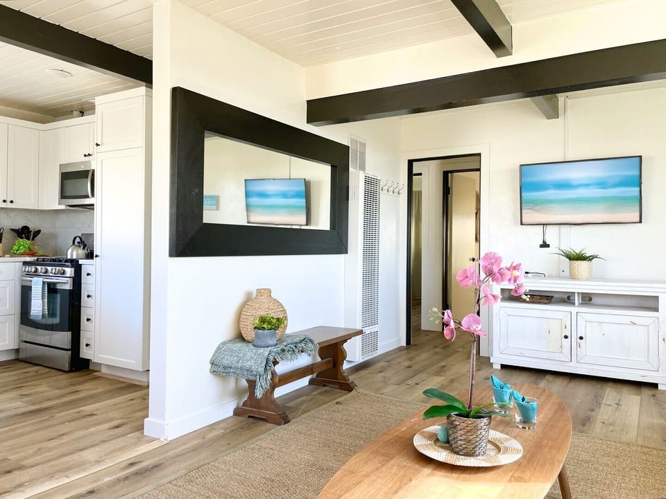 Step into your bright, coastal-inspired living space where exposed beams frame ocean artwork and fresh orchids welcome you home.