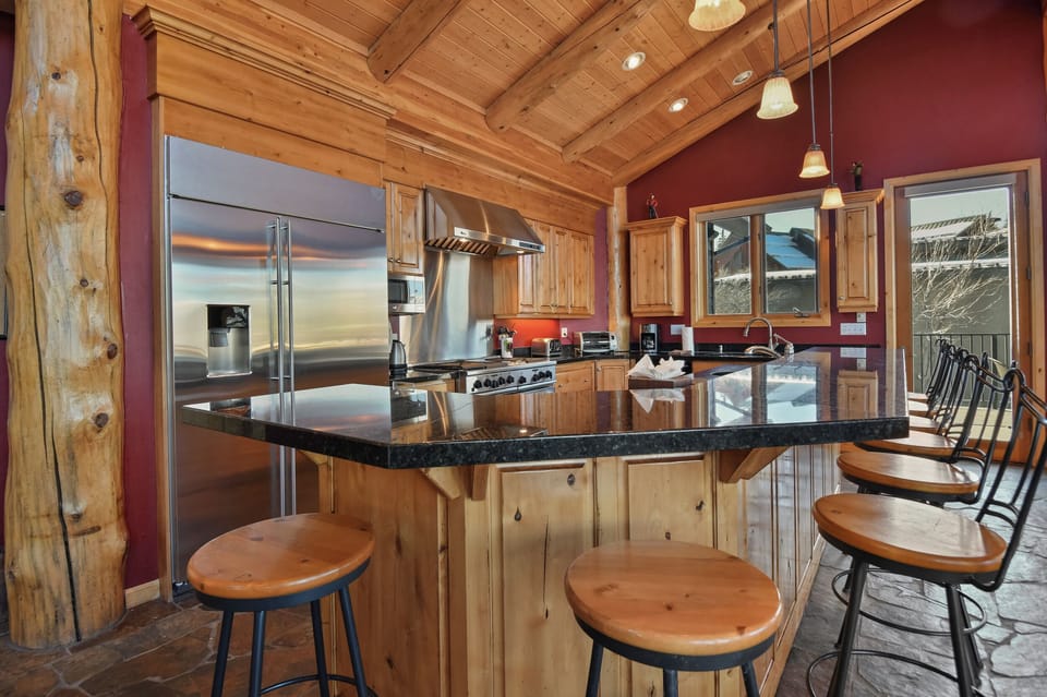 Gather around this stunning kitchen island where culinary adventures await, featuring granite countertops and stainless steel appliances under soaring wood beam ceilings.