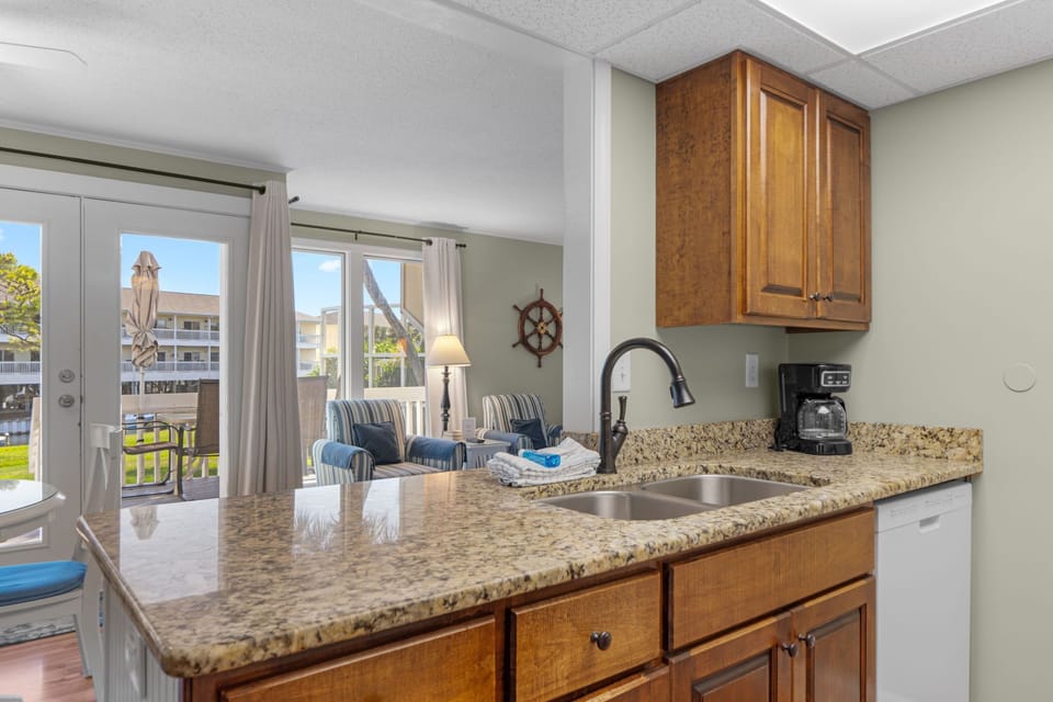 Step into your bright kitchen where granite counters and rich wood cabinets set the stage for easy meal prep, while natural light pours in and opens to a cozy living area with coastal charm.
