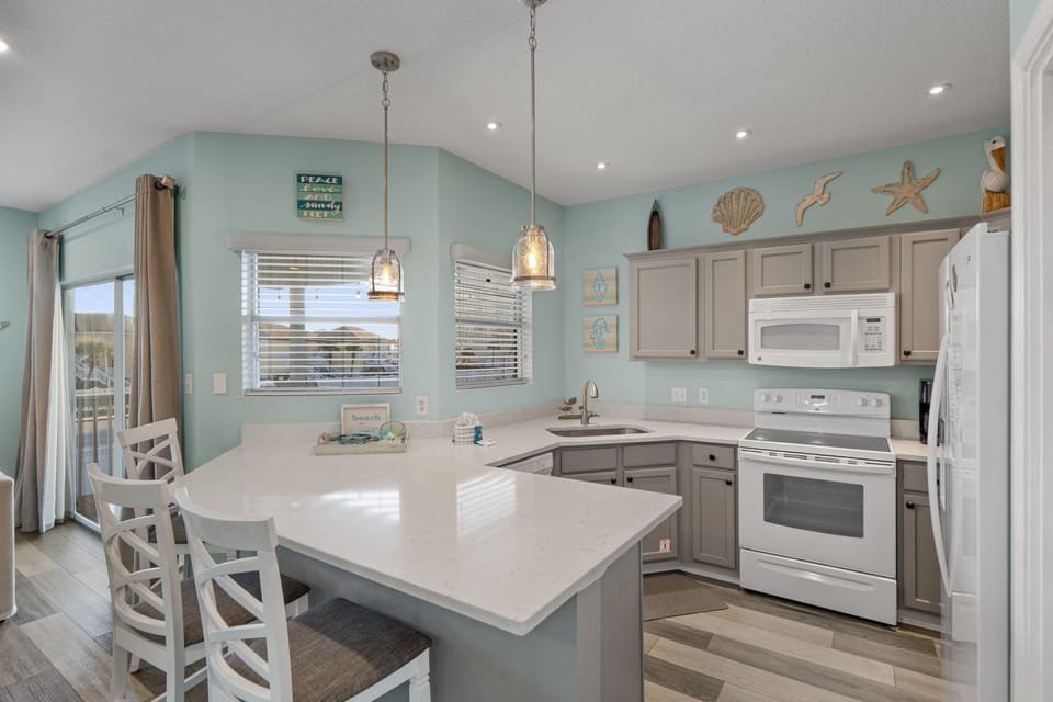 Your coastal kitchen awaits with soothing aqua walls, white countertops, and charming nautical touches that create the perfect seaside escape.