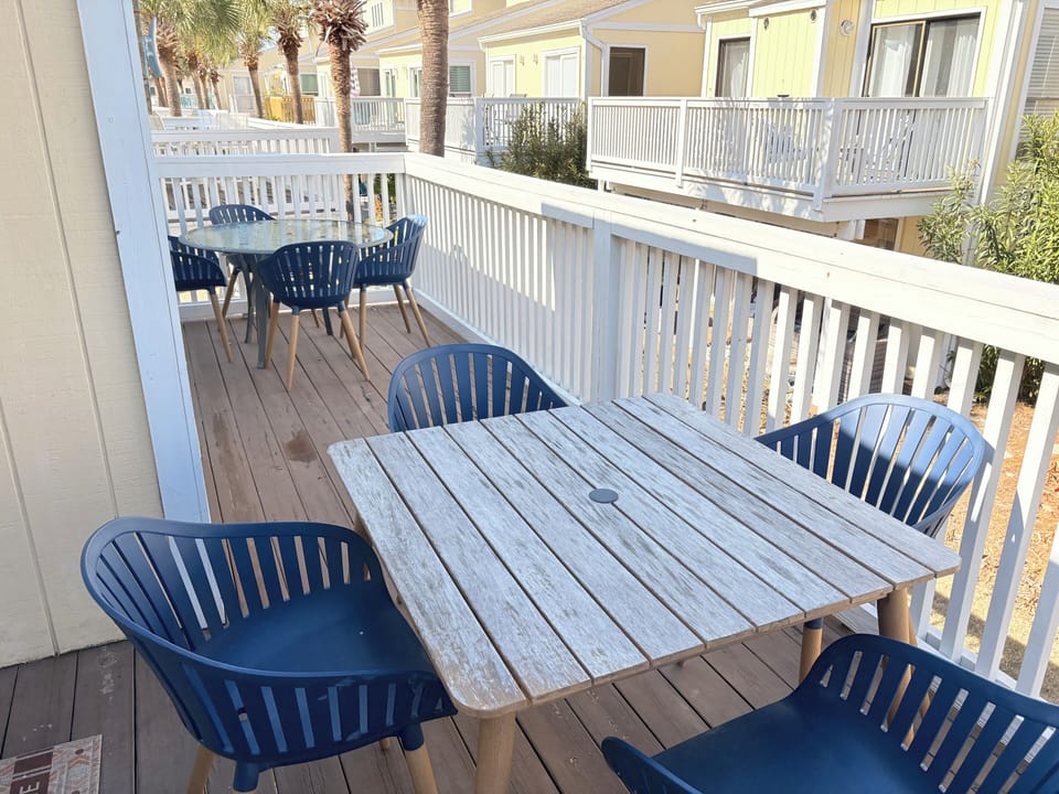 Your private deck offers peaceful outdoor dining with weathered wood tables and blue chairs overlooking tropical palm trees.