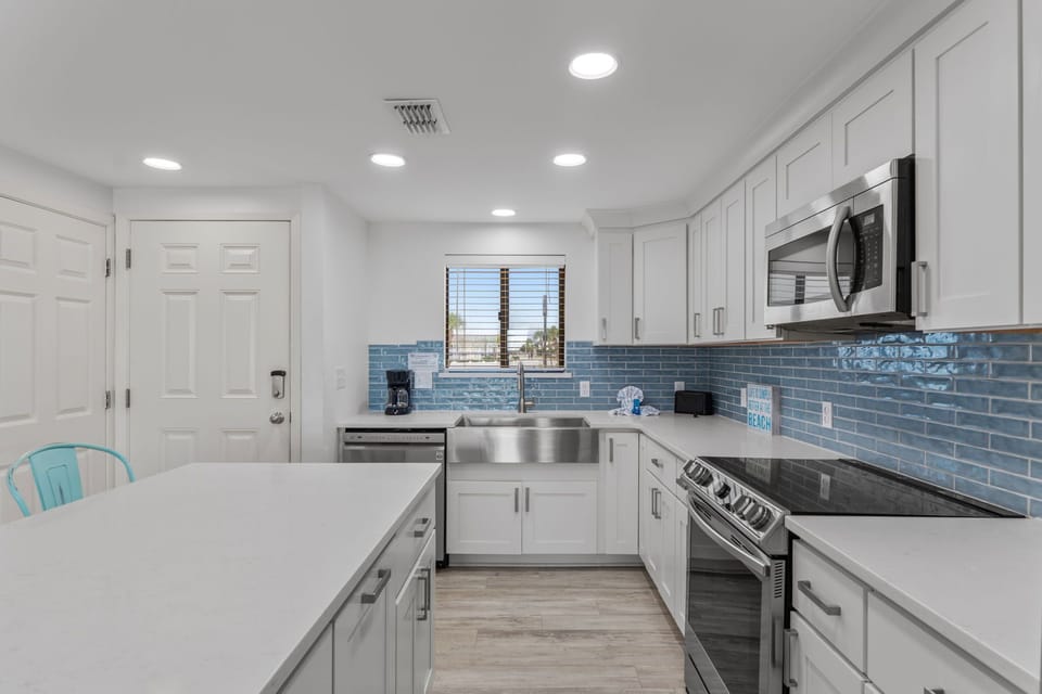 Your fully equipped kitchen awaits with modern appliances and coastal-inspired blue tile backsplash for memorable meal preparation.