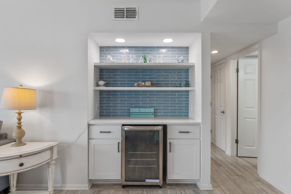 Your stylish wet bar features ocean-blue subway tiles, built-in wine fridge, and coastal decor for perfect evening entertainment.