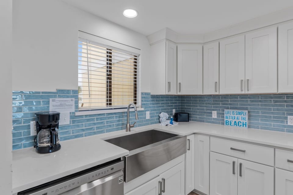 Your coastal-inspired kitchen features bright white cabinets and ocean-blue subway tiles, perfect for preparing morning coffee or seaside meals.