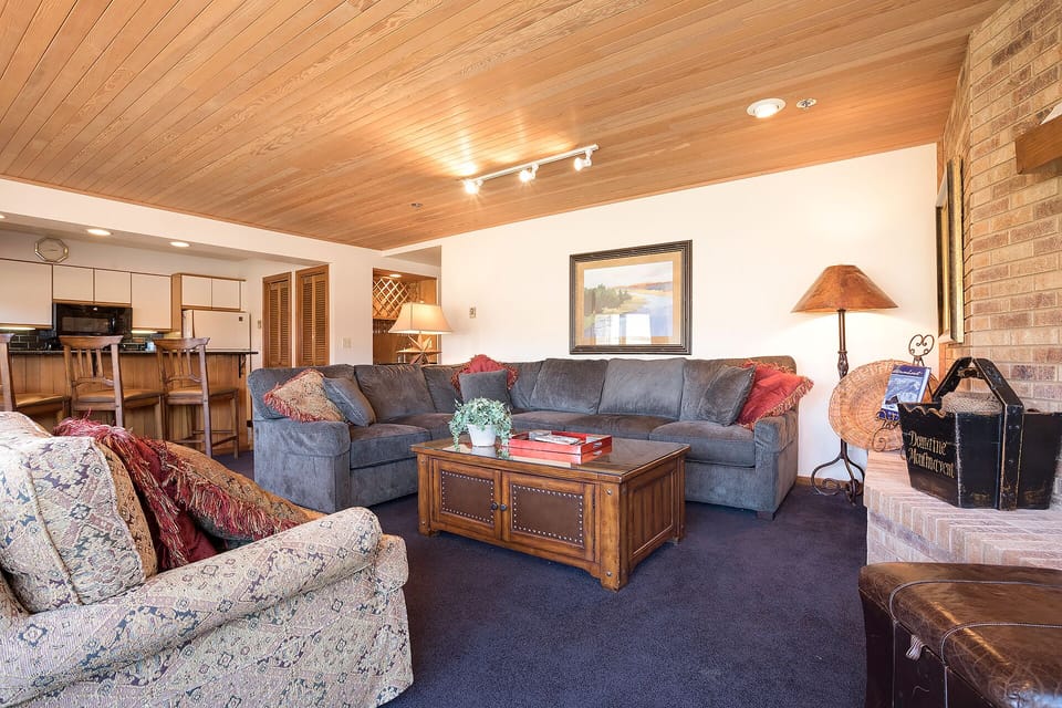 Relax in your spacious living room featuring warm wood ceilings, cozy sectional seating, and a crackling fireplace for perfect mountain evenings.