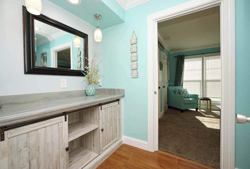 Your coastal retreat welcomes you with soothing turquoise walls and thoughtful touches like fresh florals on elegant storage.