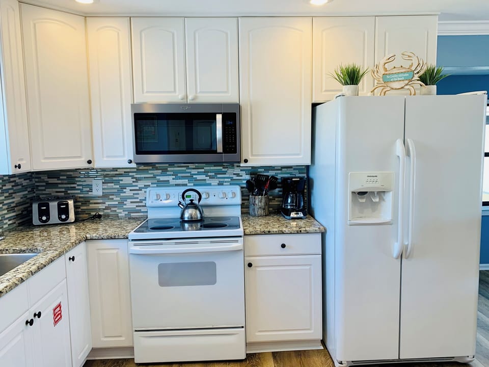 Your fully equipped kitchen awaits with modern appliances, granite counters, and coastal tile backsplash for preparing memorable meals together.
