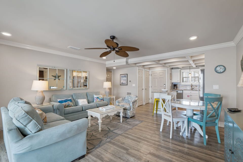 Relax in your bright, open-concept living space with cozy coastal touches and smooth hardwood floors. Sink into the plush sofas, gather around the dining table, or simply enjoy the airy flow connecting you to the kitchen.