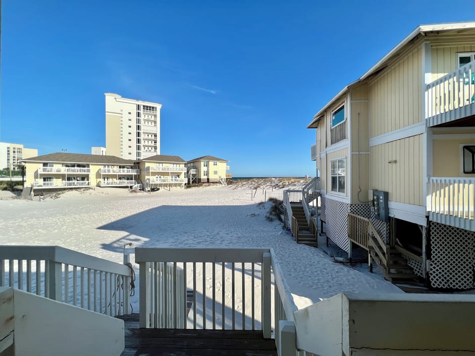 Beachfront property with pristine sandy shores and neighboring vacation rentals under clear blue skies.