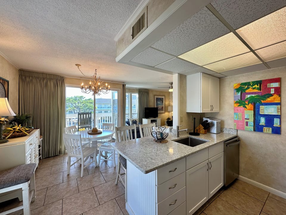 Your modern kitchen flows into a welcoming dining area, perfect for gathering with granite counters and cheerful artwork creating a warm coastal vibe.