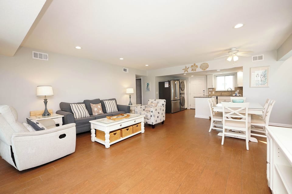 Relax in your spacious open-concept living space featuring coastal-themed decor, comfortable seating, and a fully equipped kitchen perfect for family gatherings.