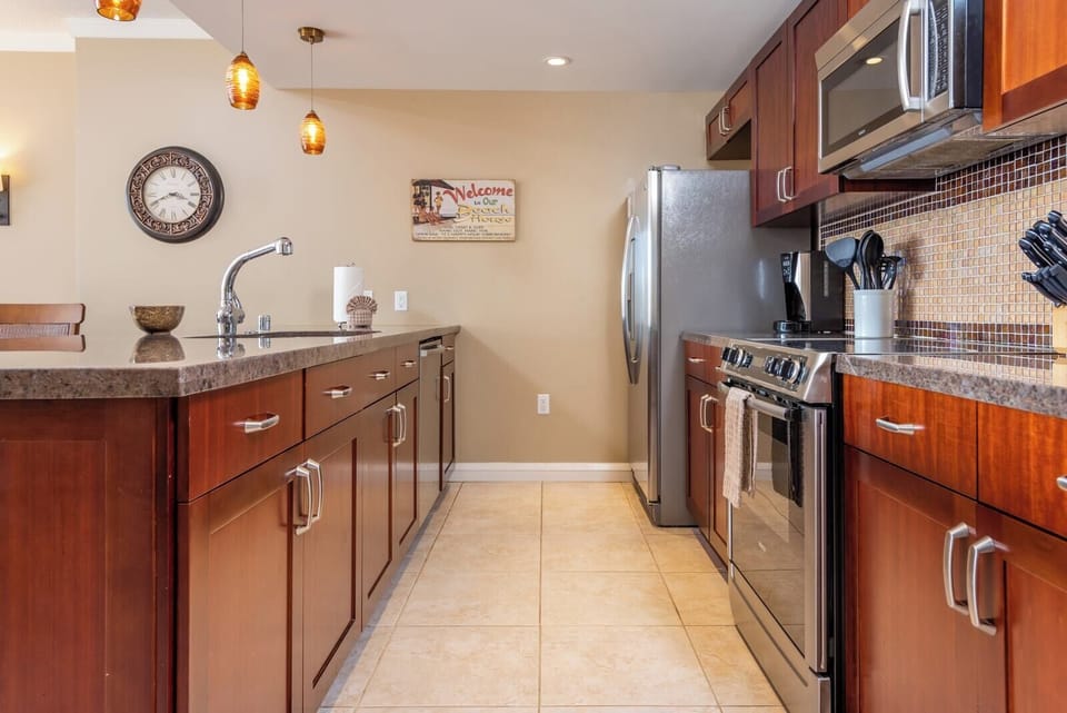 Modern island kitchen with stainless appliances, mosaic backsplash, and warm lighting. 