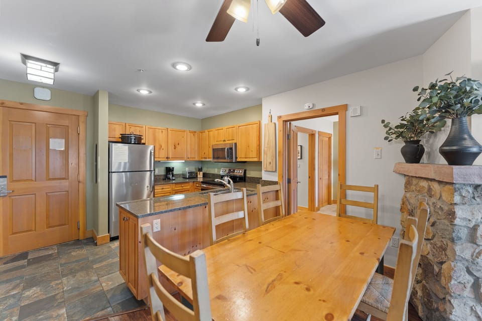 Your open kitchen flows seamlessly into the dining area, where warm wood tones and stone fireplace create the perfect gathering space.
