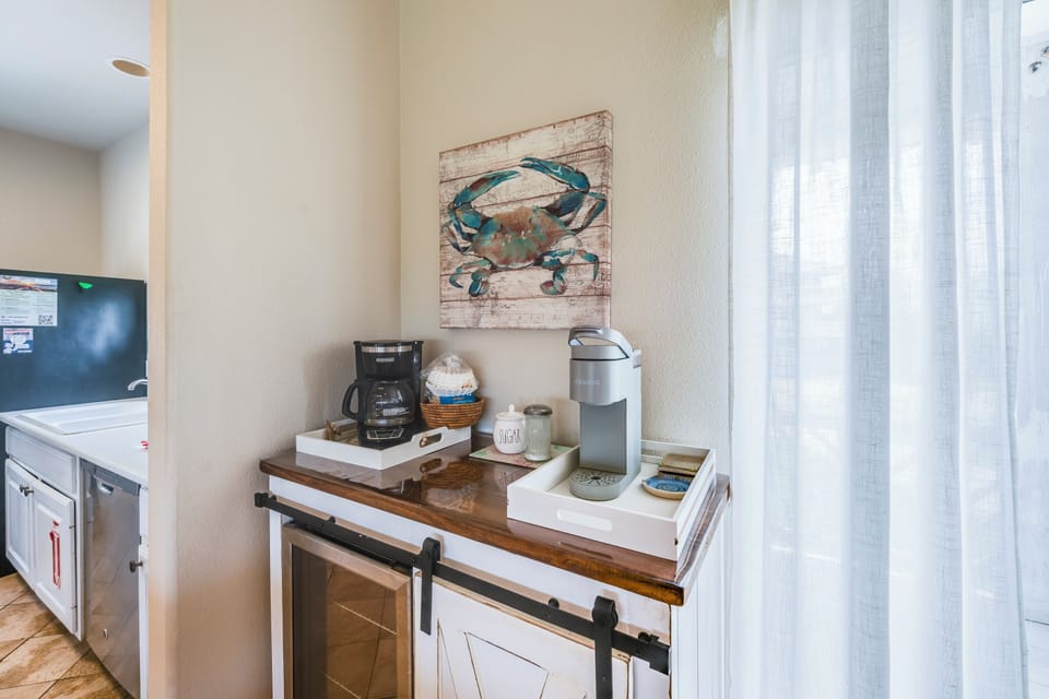 Your morning coffee station awaits with Keurig convenience and coastal charm beneath charming crab artwork.