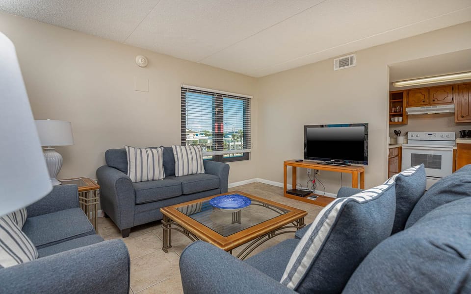 The living area features comfortable seating, a TV, and a view of the vibrant surroundings through large windows
