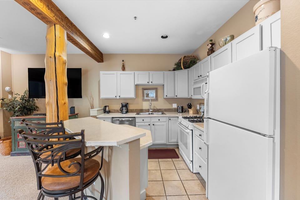 Your fully-equipped kitchen features white cabinets, modern appliances, and a breakfast bar where you'll enjoy morning coffee beneath stunning exposed beams.