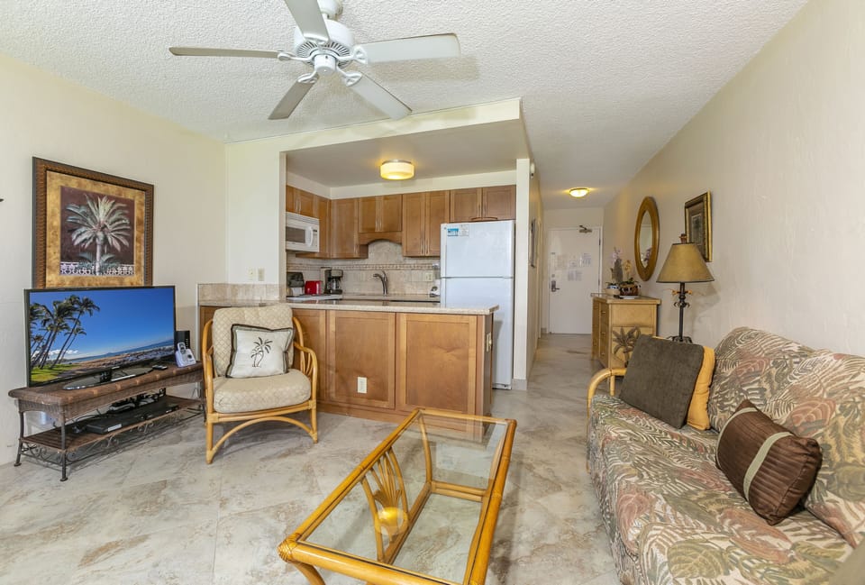 Relax in your open-concept living area with tropical-themed décor, ceiling fan, full kitchen, and flat-screen TV—perfect for unwinding after a day exploring the island.