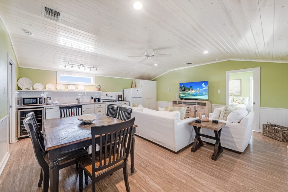 Relax in your open-concept haven where coastal charm meets modern comfort—whitewashed ceilings, plush seating, and a fully equipped kitchen create the perfect retreat.