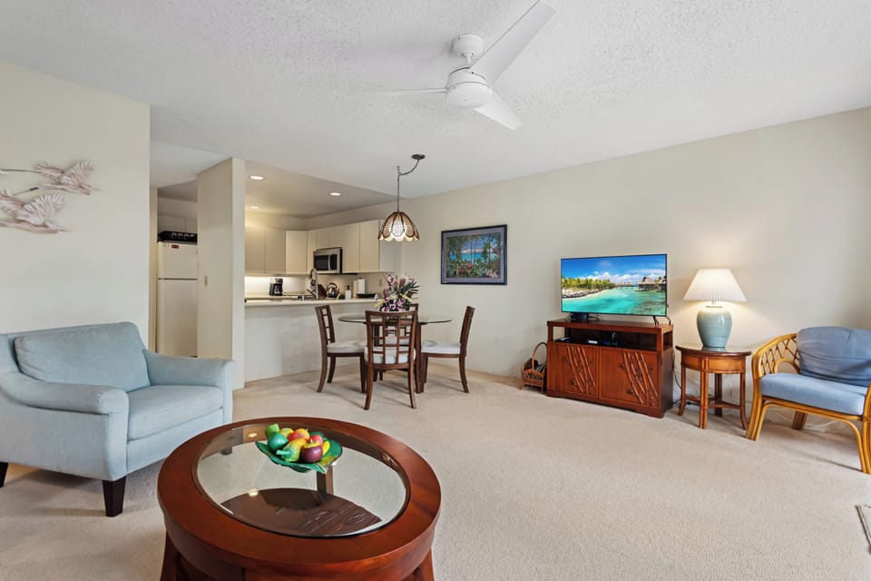 Your open-plan living and dining area blends comfort and function, with a ceiling fan overhead, coastal furnishings, and a well-appointed kitchen just steps away.