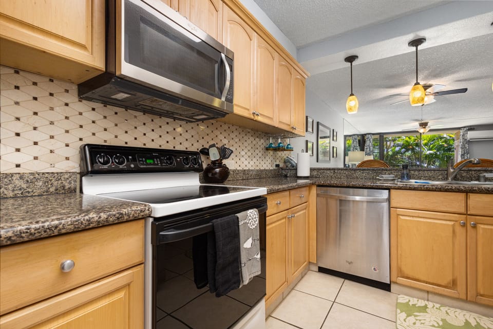 Your fully equipped kitchen features modern appliances and granite countertops, perfect for preparing meals during your stay. Natural light streams in from the living area, creating a warm and inviting space.