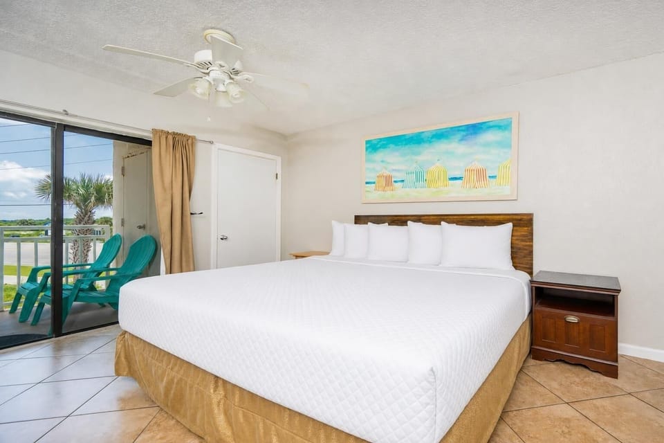 Efficiency-style bedroom featuring a plush king bed and vibrant beach-themed artwork, with access to a private balcony