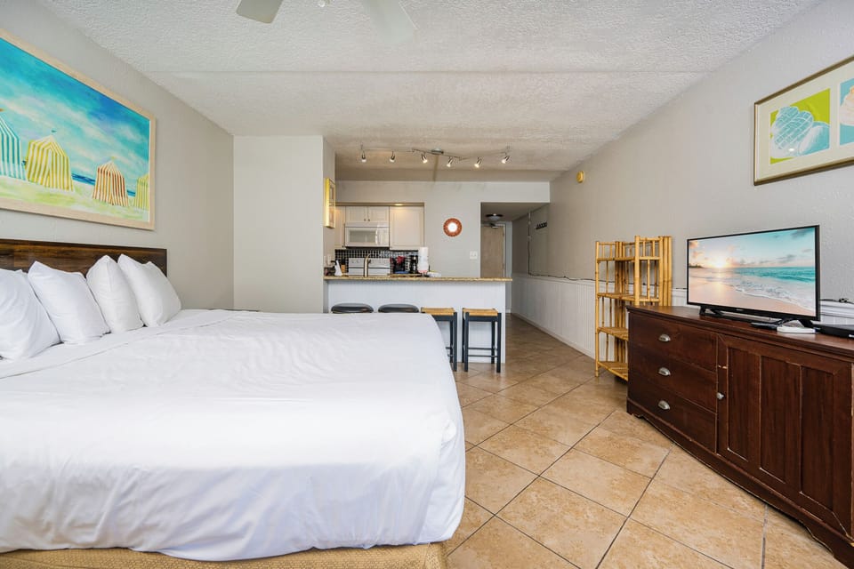 Efficiency suite featuring a plush king bed, kitchen area, and a vibrant beach-themed painting for a relaxing getaway