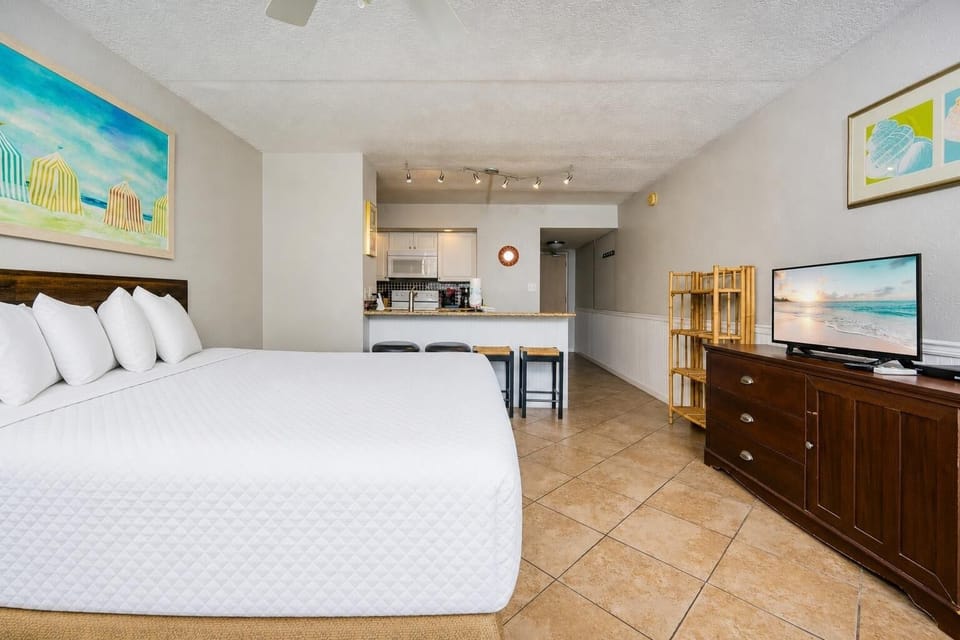Efficiency suite featuring a plush king bed, kitchen area, and a vibrant beach-themed painting for a relaxing getaway