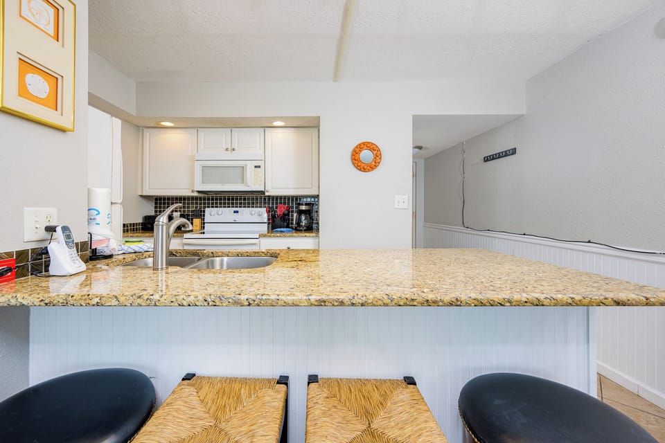 Bright kitchen featuring granite countertops, essential appliances, and inviting bar seating for a cozy dining experience
