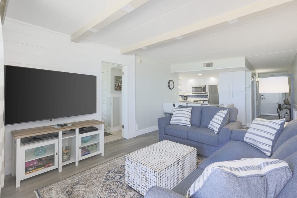 The living area features comfortable seating, a large TV, and a view into the stylish kitchen, perfect for relaxation