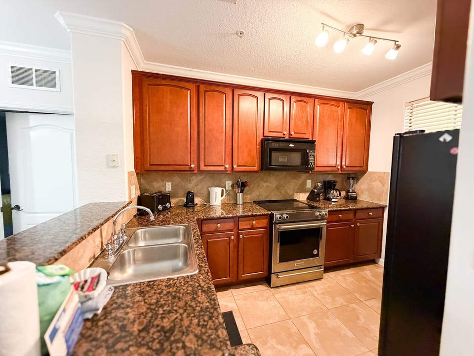 Fully equipped vacation rental kitchen with granite countertops, stainless steel oven and microwave, wood cabinetry, and modern appliances in Central Florida.