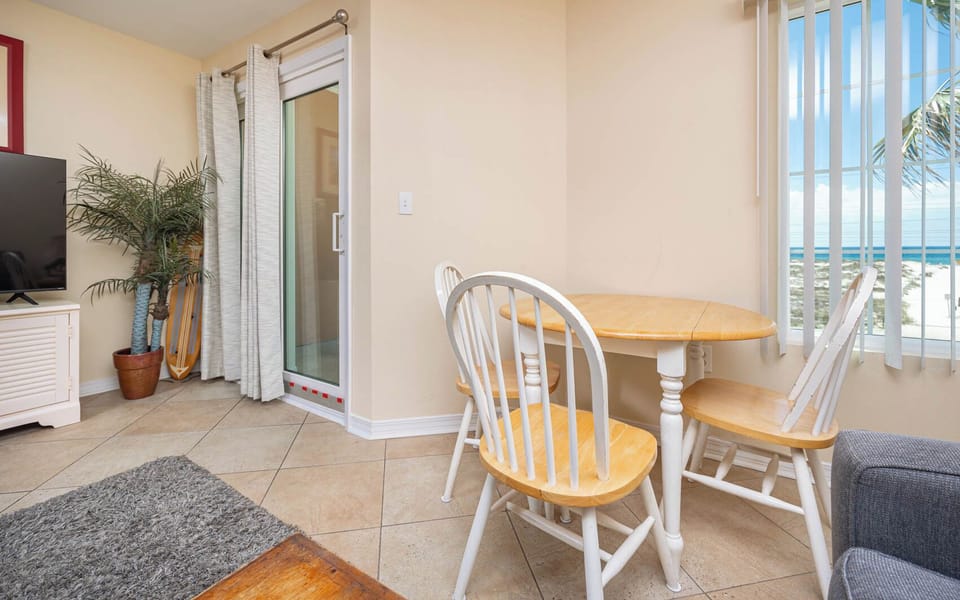 This cozy dining area features a round wooden table, a TV, and a stunning beach view through large windows